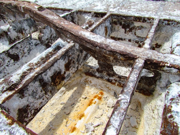Large-format photograph: Close-up view of a removed Crawlerway Grid Panel, showing Top Chord construction (and corrosion damage) in area where concrete fill has been chipped out of the Panel with enough detail visible to determine that the Panels, as originally fabricated and installed, did not match the as-built contract drawings which were submitted and approved at the time (1960's), resulting in a condition where subsequent modifications work would become especially difficult, resolving the discrepant conditions in a timely manner, to everyone's satisfaction. Photo credit: Withheld by request. Large-format photograph: Close-up view of a removed Crawlerway Grid Panel, showing Top Chord construction (and corrosion damage) in area where concrete fill has been chipped out of the Panel with enough detail visible to determine that the Panels, as originally fabricated and installed, did not match the as-built contract drawings which were submitted and approved at the time (1960's), resulting in a condition where subsequent modifications work would become especially difficult, resolving the discrepant conditions in a timely manner, to everyone's satisfaction. Photo credit: Withheld by request.
